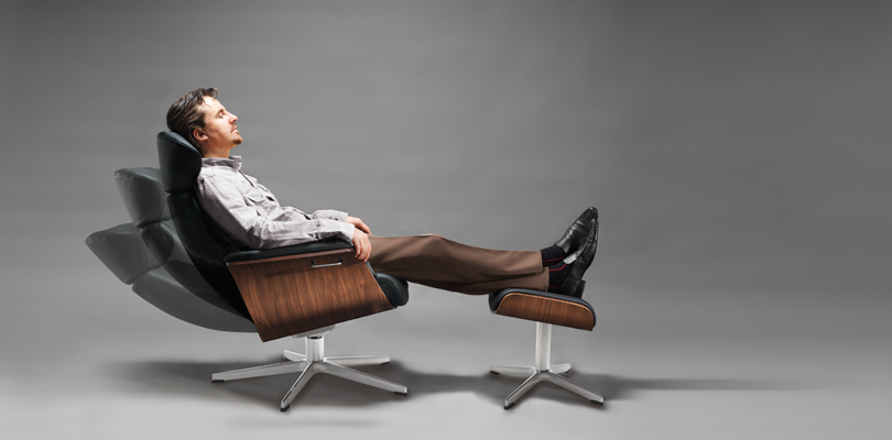 Das Foto zeigt die Funktion der absenkbaren Rückenlehne eines TIMEOUT Sessels mit Hocker, in dem eine Person sitzt